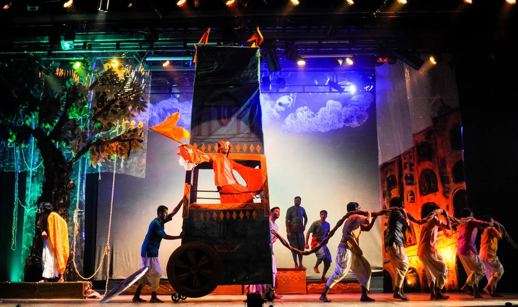 A full company pulling a painted cart across a lit stage