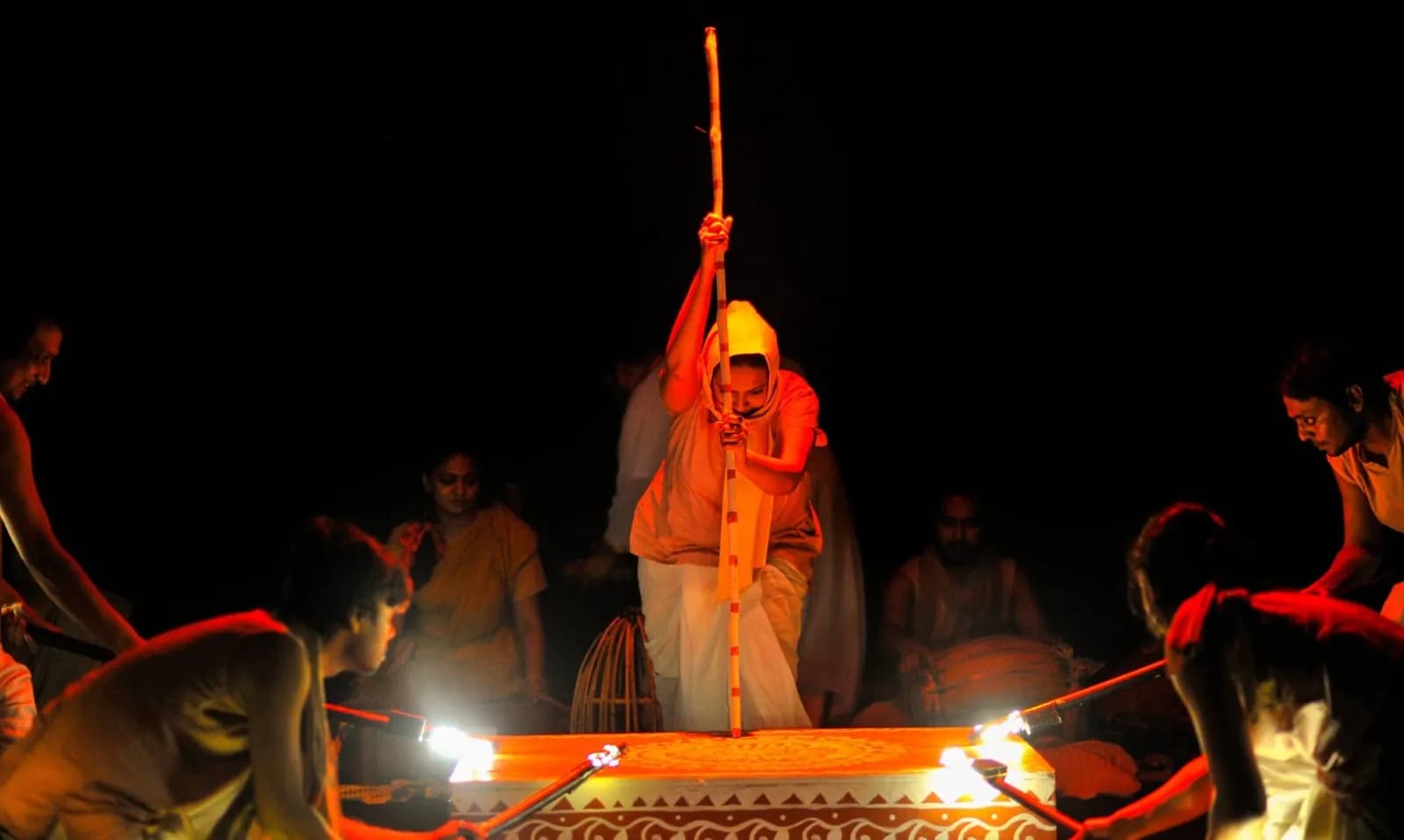 A folk performer with a raised staff at a lantern-lit circle of musicians