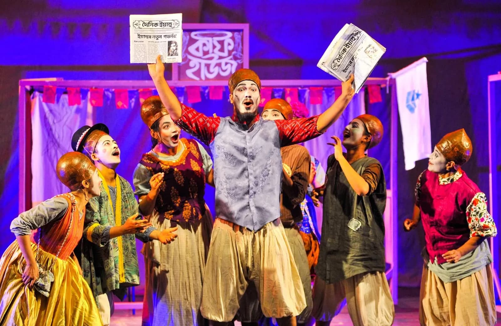 A masked ensemble holding newspapers aloft under violet light